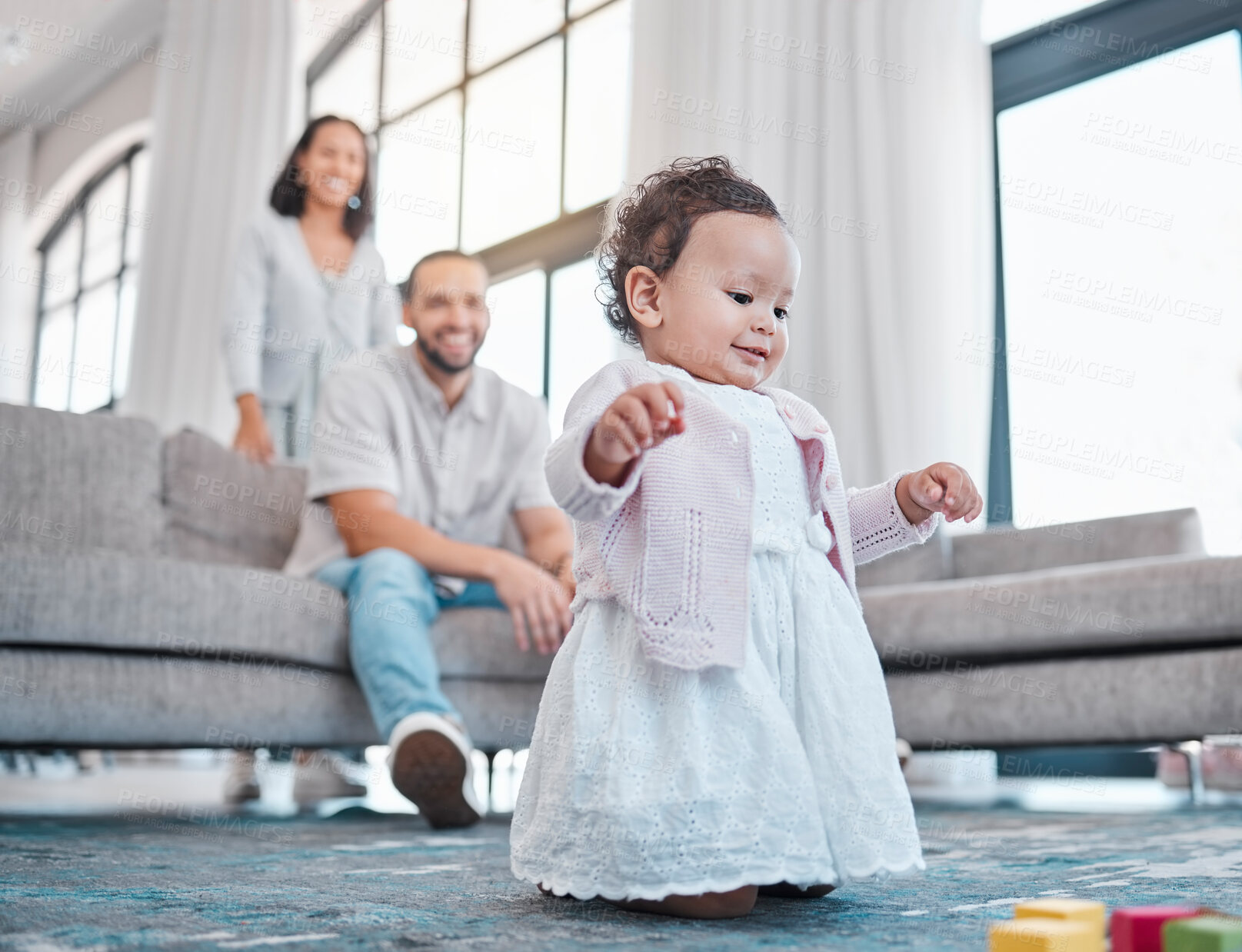 Buy stock photo Baby, family and love with a girl learning or walking in the living room of her home with parents watching. Kids, floor and walk with a daughter taking her first steps with mom and dad in the house