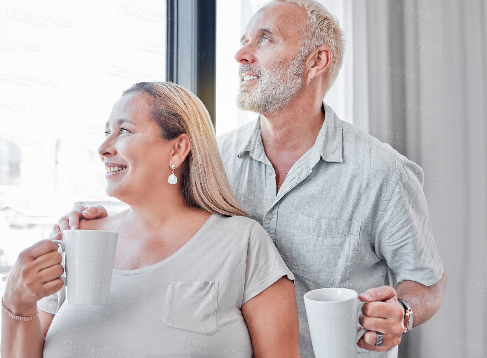 Buy stock photo Elderly couple, hug and coffee by window with smile in contemplation, vision or morning routine at home. Happy senior man and woman smiling looking out glass while enjoying a warm drink together