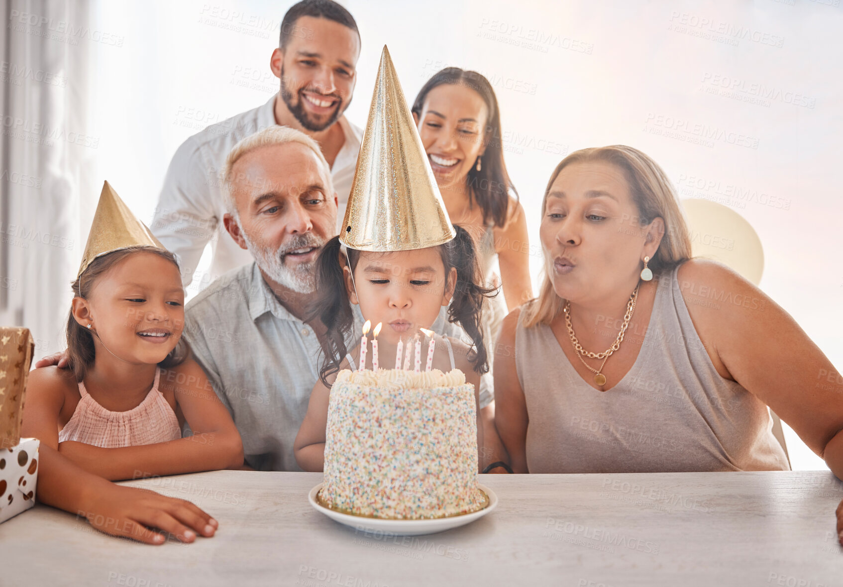 Buy stock photo Birthday, family and girl blowing candles on cake with party hats, parents and grandparents in home. Happiness, big family and happy young child make a wish on festive celebration and birthday party