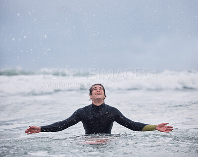 Surfing, sports and man in ocean during rain enjoy nature, spring weather and swimming in waves. Happiness, raining and young male surfer in sea doing watersports for exercise, training and fitness