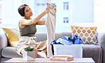 Laundry, housekeeping and woman folding clothes, cleaning and working in the living room of her house. Routine, washing and cleaner with clean clothing in a basket on the sofa of the home lounge