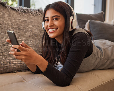 Buy stock photo Woman, smile and phone listening to music with headset while relaxing on living room sofa. Portrait of happy female in relax and enjoying audio track, chatting or texting on smartphone on the couch