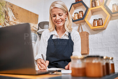 Buy stock photo Laptop, small business and senior woman writing notes while doing inventory or online marketing. Happy, smile and elderly entrepreneur in a honey store working on admin or shop sales with a computer.