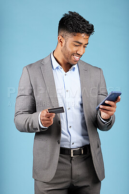 Buy stock photo Credit card, online banking and man with phone in studio on blue background using smartphone for payment. Internet banking, ecommerce and Indian man with bank card for online shopping on mobile app