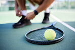 Tennis ball, racket and man tie shoes on tennis court preparing for competition, game or match. Exercise, fitness and tennis player getting ready for practice, training or workout outdoors on field.