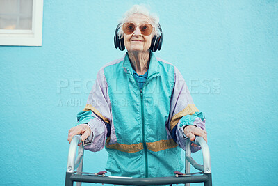 Buy stock photo City, fashion and senior woman with headphones listening to music, audio and radio on blue background wall. Freedom, style and elderly female with modern, urban and trendy clothes with walker in town