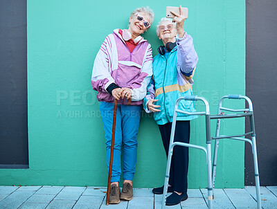 Buy stock photo Phone, selfie and disability with senior friends posing for a photograph outdoor on a green wall background. Happy, mobile and walker with a mature woman and friend taking a picture together