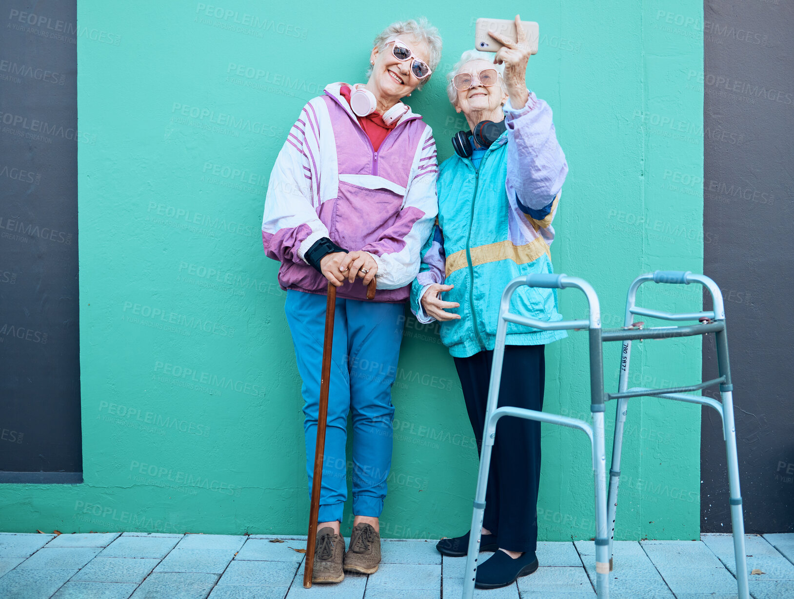Buy stock photo Phone, selfie and disability with senior friends posing for a photograph outdoor on a green wall background. Happy, mobile and walker with a mature woman and friend taking a picture together