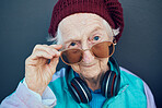 Senior woman, face and fashion sunglasses, vintage and  90s clothes, cool style and headphones with attitude against a wall outdoor. Elderly model, edgy attitude and retro portrait or retirement