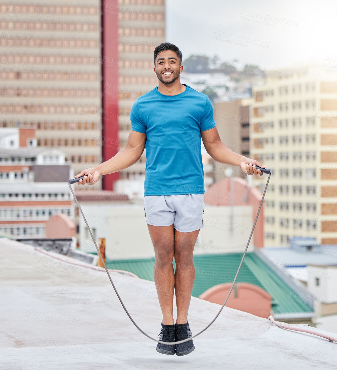 Buy stock photo Jump rope, fitness and portrait of a man on a rooftop, sports training and cardio in the urban city. Energy, jumping and athlete skipping for wellness, workout and strong body with happiness
