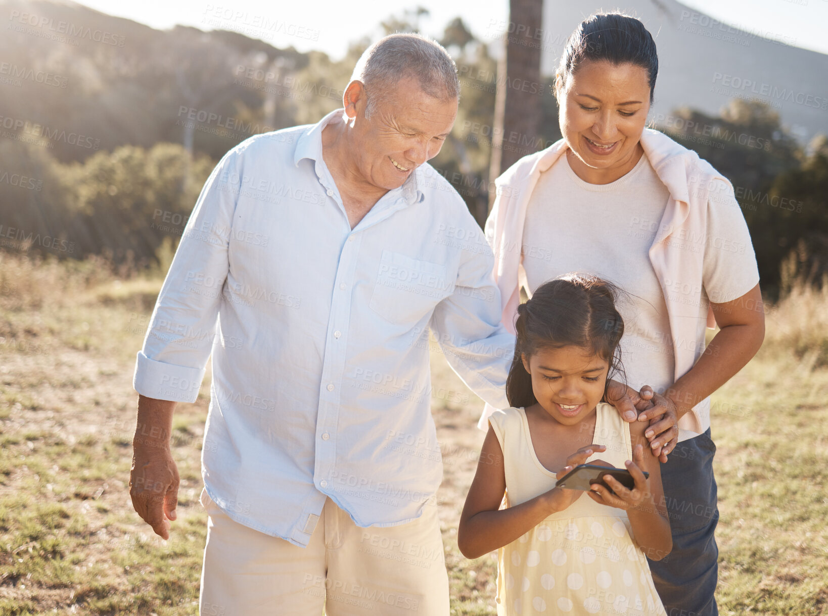 Buy stock photo Phone, family and nature with a girl and grandparents outdoor together during summer vacation. Social media, love and care with a senior man and woman bonding with their female grandchild outside