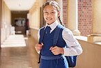 Education, school and portrait girl in a uniform with a backpack standing in the hallway for class. Happy, smile and child student in the corridor for classroom to learn or study knowledge at campus.