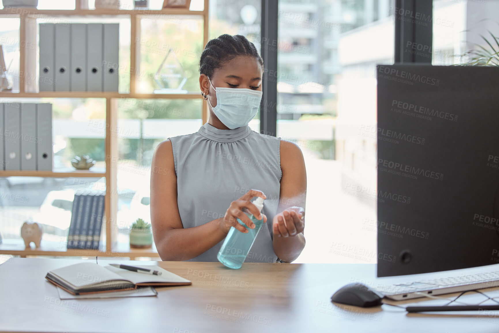 Buy stock photo Covid, mask and hand sanitizer with a business black woman cleaning while working in her office. Health, safety and sanitizing with a female employee using disinfectant during the corona virus