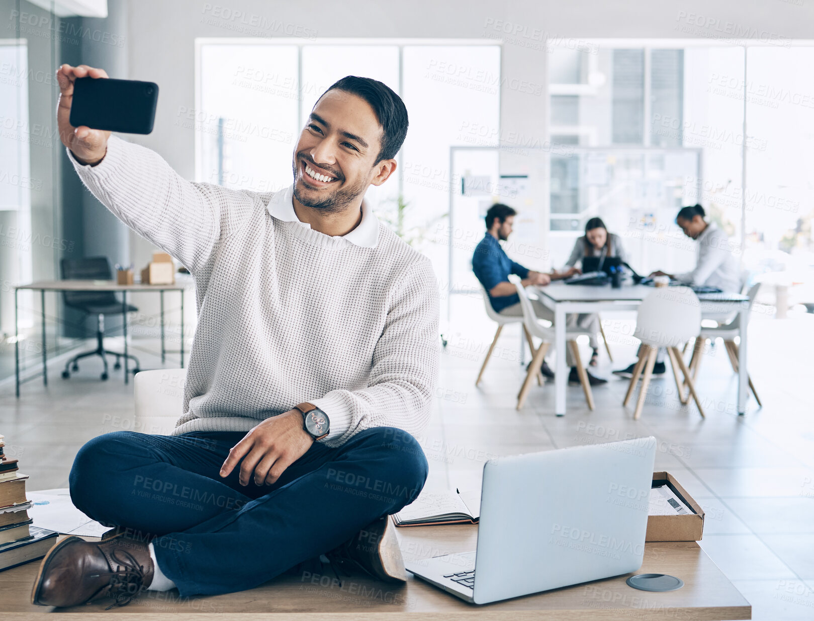 Buy stock photo Selfie, phone and businessman sitting on desk in meeting with team, staff and working in corporate office. Startup, happiness and young Asian male worker using smartphone to take picture in workplace