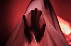 Hand, fabric and red with a person under a sheet in a bedroom or studio on a red background for psychology. Hands, silhouette and shadow with an adult struggling with mental health, anxiety or fear