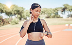 Music, earphones and runner woman pulse check on workout, training and athlete break. Wellness, fitness and running girl pause at stadium track for performance analysis on smartwatch app.