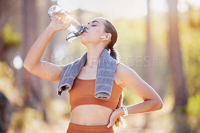 Fitness, woman and drinking water after running, training and cardio exercise in a forest. Sports, water and girl drinking after run in nature with music, podcast or radio for audio track by runner