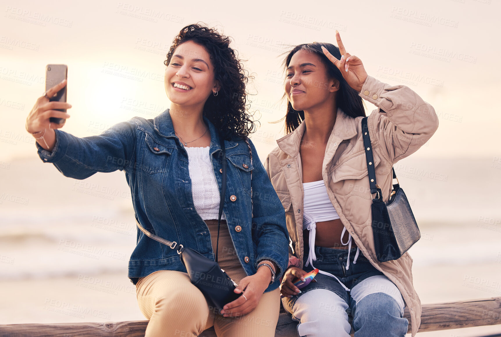 Buy stock photo Selfie, peace sign and women with phone, beach and relax outdoor for fun, travel and smile together. Female friends, young girls and sunset with smartphone, hand gesture and social media to connect.