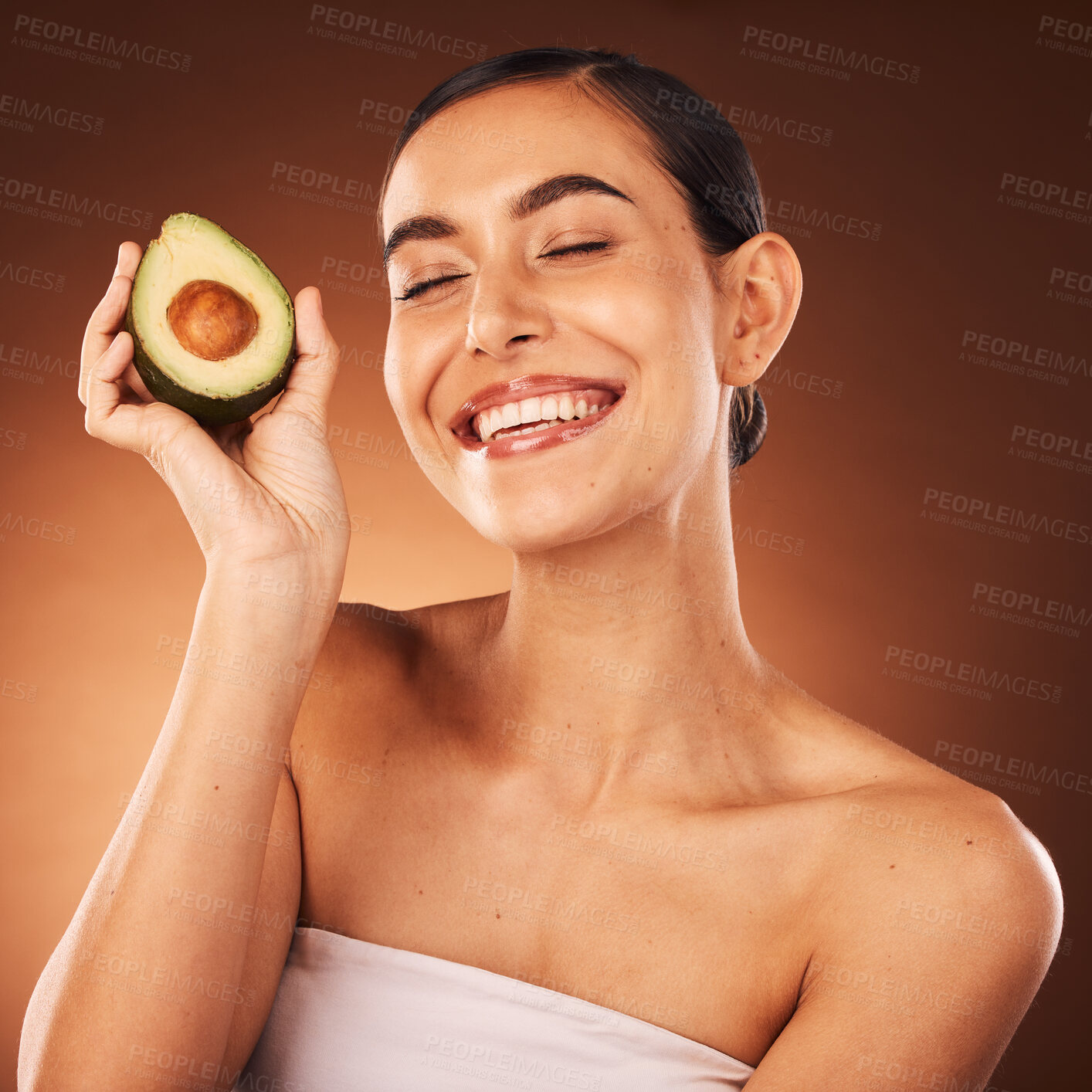 Buy stock photo Face, skincare and avocado with a model woman in studio on a brown background to promote healthy eating. Food, health and wellness with an attractive young female inside for luxury or natural care