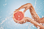Hands, water splash and grapefruit cosmetic skincare for vitamin c nutrition, citrus health treatment and natural wellness. Healthy skin hygiene, advertising hydration and a blue studio background 

