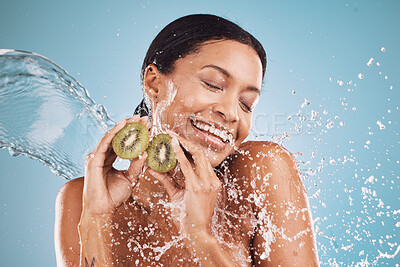 Buy stock photo Woman, kiwi and water splash for skincare, cosmetics and natural beauty on blue studio background. Wet, young female and black girl fruit for wellness, clear or smooth skin for health, smile or relax