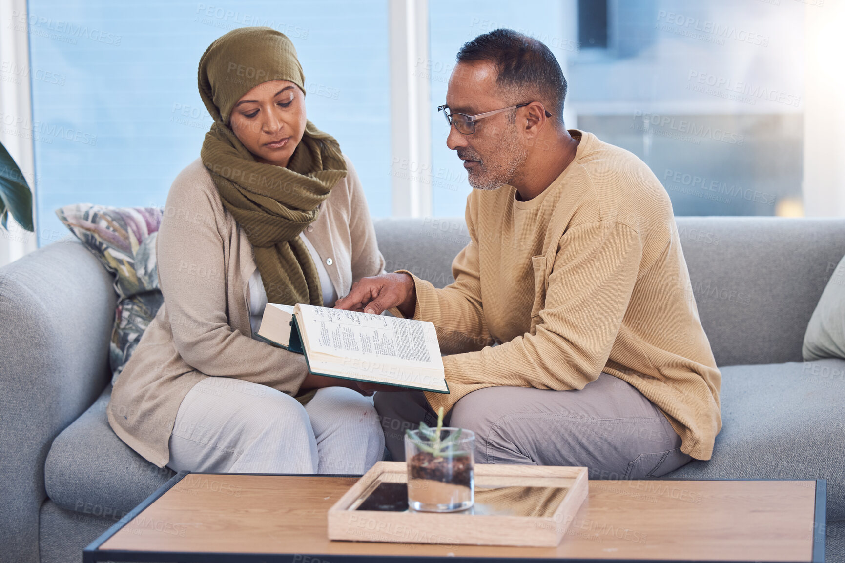 Buy stock photo Muslim couple, bonding and reading book, holy koran or traditional prayer quran on sofa in house or home living room. Islamic man, middle aged woman and mature people in muslim pray for eid mubarak