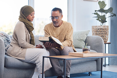 Buy stock photo Worship, muslim and couple reading the quran for gratitude on sofa in their living room together. Islam, retirement and senior man and woman with a hijab studying the islamic religion during ramadan.