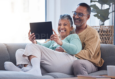 Buy stock photo Tablet, love and relax with a senior couple sitting on a sofa in the living room of their home together. Funny, joke and humor with a mature man and woman laughing while watching a comedy in a house