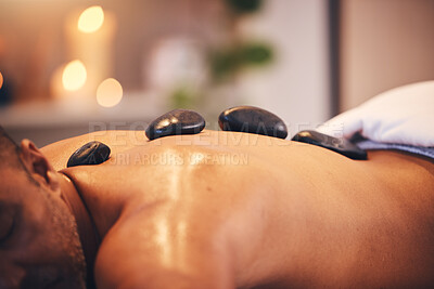 Buy stock photo Massage, hot stone and relax with a man in a spa, lying on a table or bed for physical therapy at a luxury resort. Wellness, rock and zen with a male customer relaxing in a health center for rest
