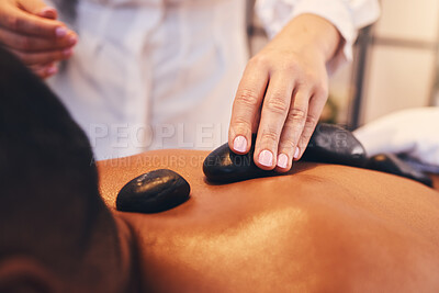 Hands, hot stone and massage with a man in a spa, lying on a table or bed for stress relief and wellness. Relax, luxury and rock with a male customer in a health salon for physical therapy