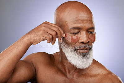 Buy stock photo Skincare, eye patches and senior man doing wellness, health and natural face routine in studio. Cosmetic, beauty and elderly African guy doing self care facial treatment isolated by purple background