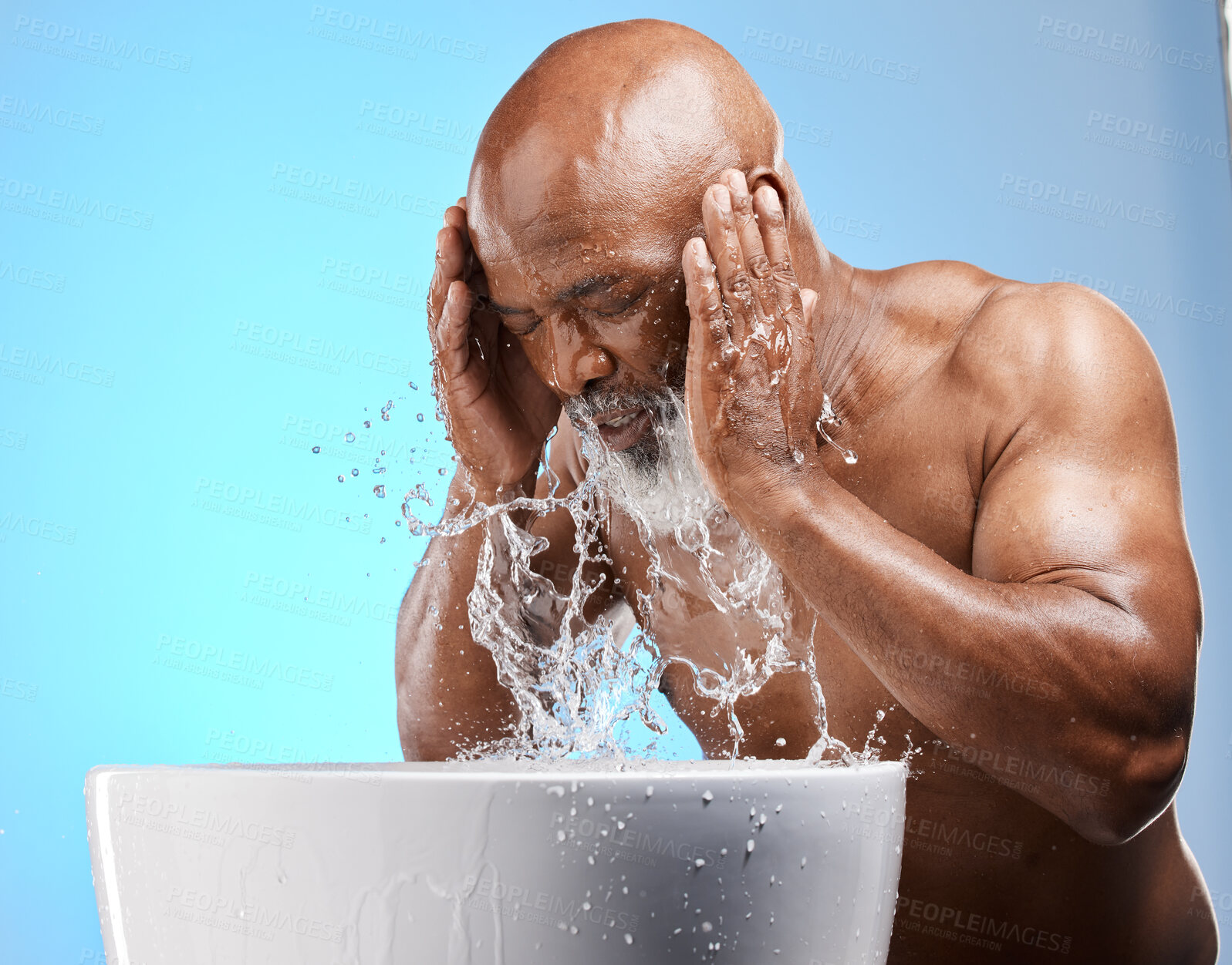 Buy stock photo Skincare, water splash and black man for senior skincare while washing face for a glow, healthy and clean skin on blue background. African model in studio with basin for dermatology and self care