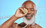 Skincare, kiwi and senior man in studio for beauty, water splash and wellness on blue background mockup. Beauty splash, fruit and water with elderly man cleaning, happy and relax with nature product