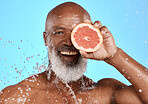 Portrait, skincare or black man with grapefruit studio with water splash on blue background with mockup space. Smile, face or senior male model on healthy diet for beauty, detox or vitamin c benefits