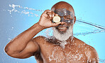 Face, water splash and senior black man with lemon and clay mask in studio isolated on a blue background. Portrait, cleaning and hygiene of elderly male model with fruit for nutrition and vitamin c.