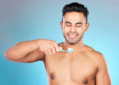 Buy stock photo Teeth, dental care and man brushing teeth with toothbrush and toothpaste on blue background with smile on face. Morning routine, healthcare and fresh, happy male model from India in studio portrait.