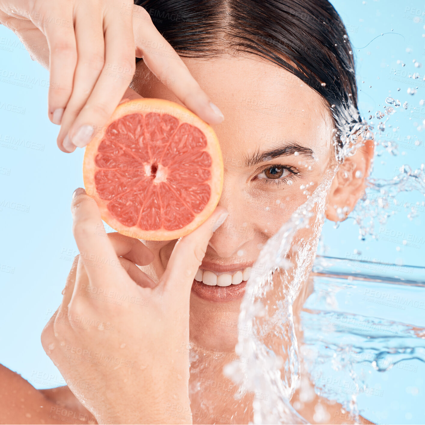 Buy stock photo Face, water splash and woman with grapefruit, shower or skincare with happy smile, vitamin c or cleaning body. Female model, fruit or wellness in blue studio background with skin care or healthy skin