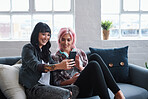 Two women friends using smartphones sitting on sofa at home watching entertainment on mobile phones