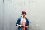 Portrait young man using smartphone listening to music wearing headphones with concrete wall background