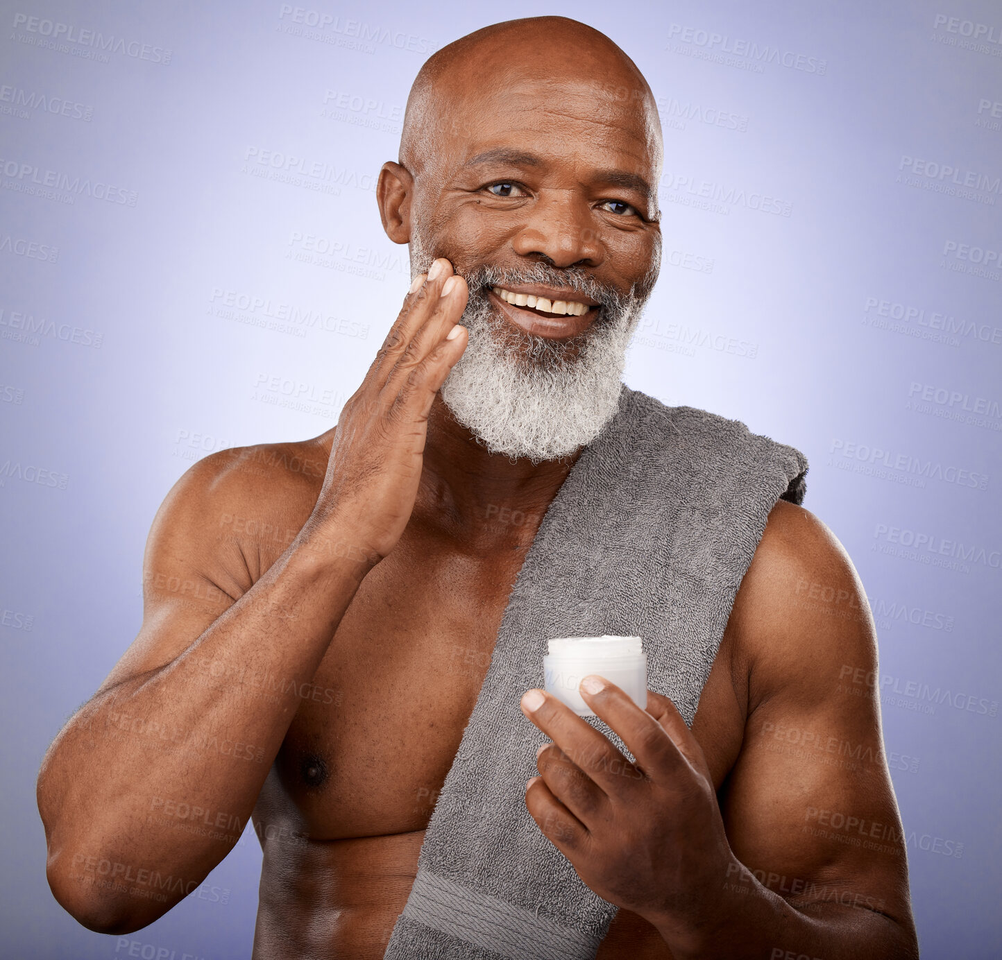 Buy stock photo Skincare, beauty cream and black man studio portrait with a towel and lotion for cosmetics, self care and dermatology product on a purple background. Face of black male with a smile for healthy skin 