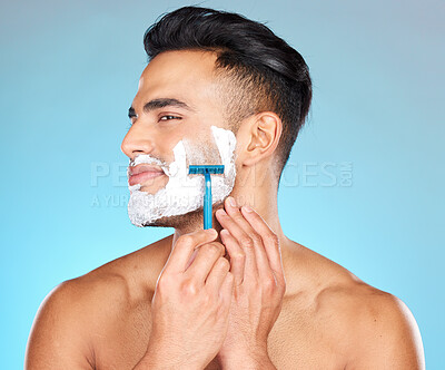 Buy stock photo Studio, skincare and man shaving beard with razor blade for beauty wellness, grooming or self care on blue background. Hair removal, face or model cutting facial hair in morning routine with product 