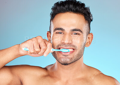 Face portrait, dental and man brushing teeth in studio isolated on a blue background. Wellness, oral health and routine of happy male model holding toothbrush for hygiene, oral care and dental care.
