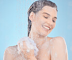 Face, beauty and woman in shower in studio isolated on a blue background. Water splash, cleaning and female model from Canada washing or bathing with sponge or loofah for wellness, health or skincare