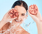 Portrait, skincare and pomegranate by woman in water splash for wellness, cleaning and skin health on blue background. Beauty, splash and fruit product by girl model smile for vegan facial in shower