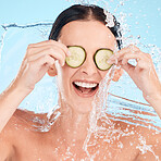 Water, beauty and cucumber with a woman in the shower in studio on a blue background for hygiene or hydration. Health, wellness and luxury with an attractive young female in the bathroom for skincare