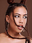 Makeup, hair and woman biting braid with edgy hairstyle and beauty on a brown studio background. Trendy, cosmetics and cosmetic haircare with braided hair style and cool eyeliner on a studio backdrop