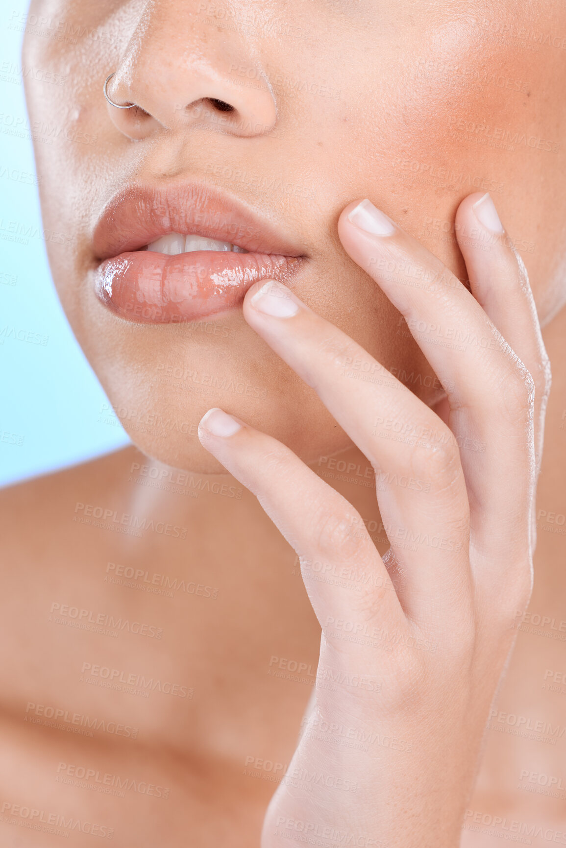 Buy stock photo Hand, lips and skincare with a model woman touching her face or cheek in studio on a blue background for cosmetics. Mouth, skin and fingers with a female posing to promote a natural treatment product