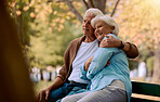 Couple, elderly and hug in park during retirement, sitting on park bench with love and spending quality time outdoor. Happy, trust and support with marriage, senior man and woman retired in New York.
