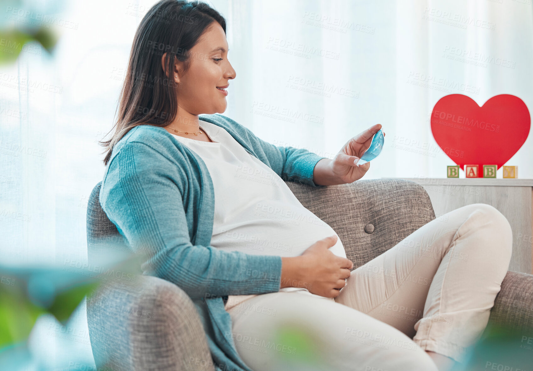 Buy stock photo Pregnant woman, ultrasound and mother on sofa in home looking at picture. Pregnancy, sonography and happy female in house with photograph, sonogram and love, care and affection for baby in stomach.