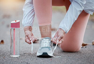 Senior woman fitness, exercise and shoes with hands tying laces while running on a concrete road or street. Workout, training and cardio with a elderly female hand getting ready for a run routine